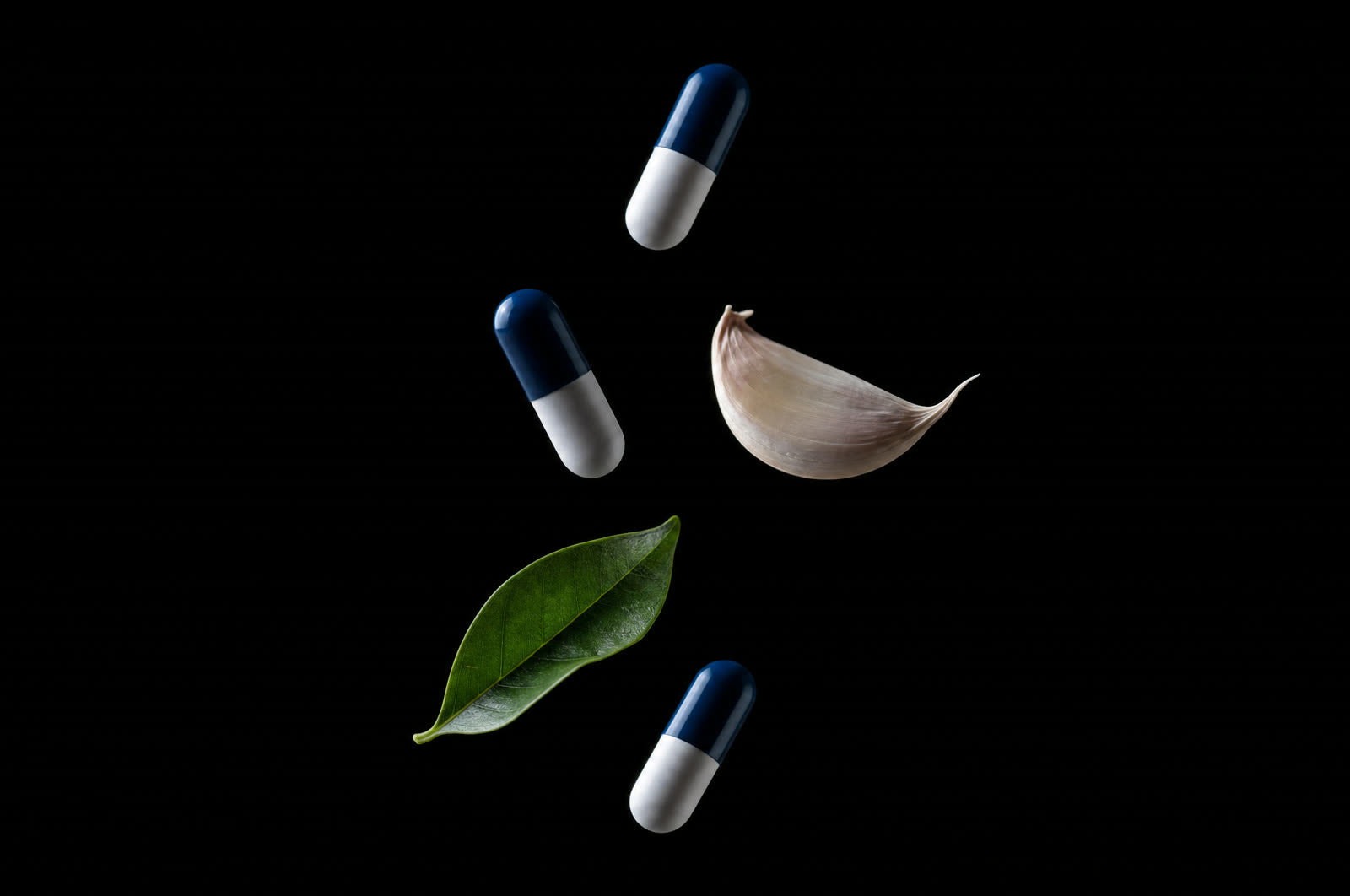 Capsules, a garlic clove, and a tea leaf suspended in darkness